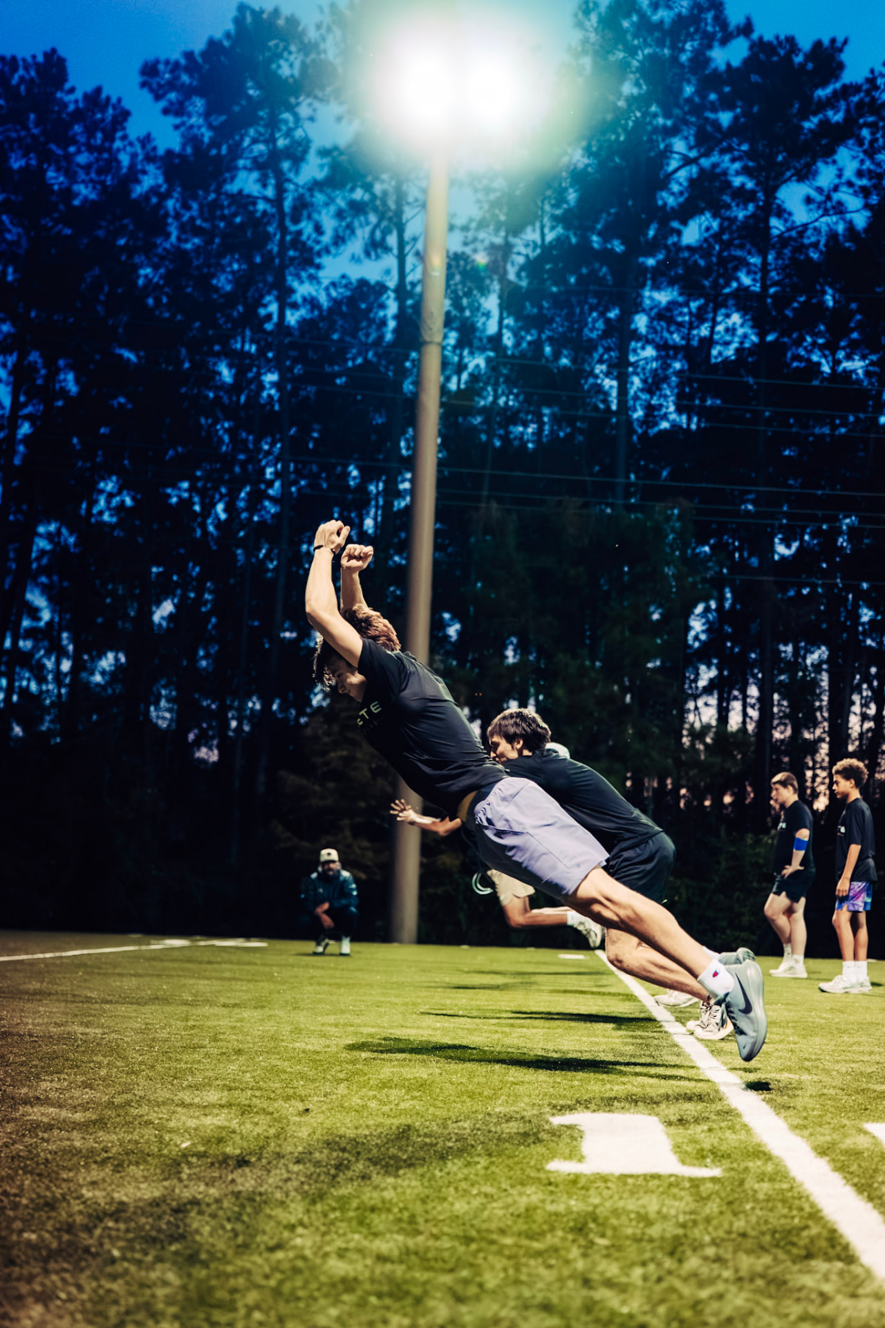 Athletes accelerating across the turf under the training lights